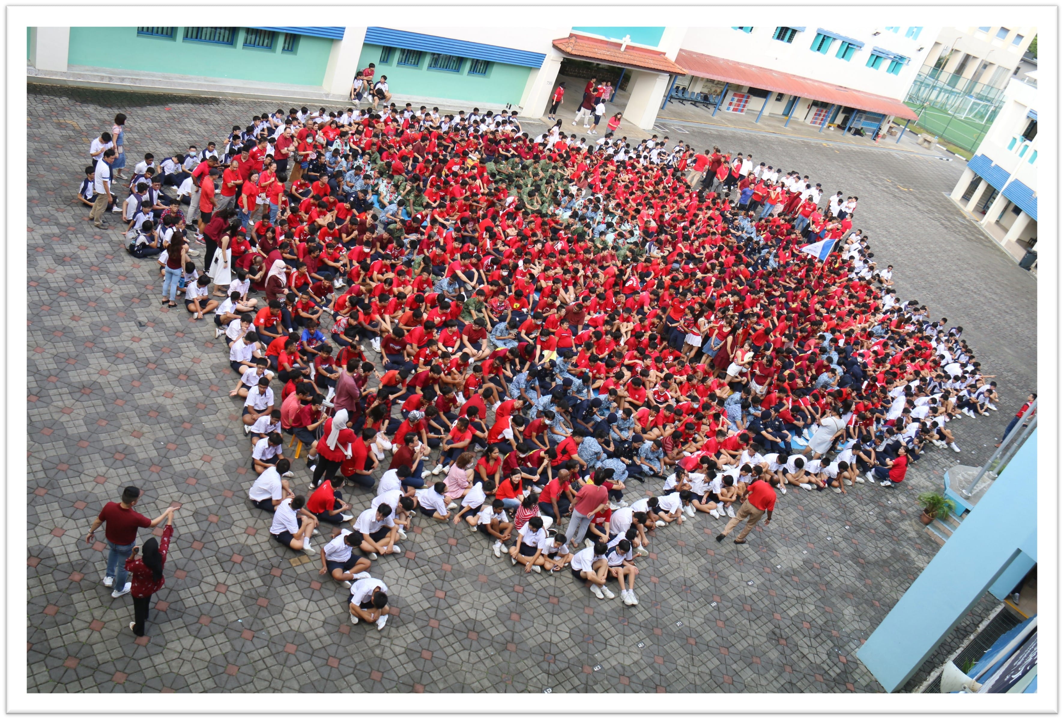 Hundreds of students in red and white uniforms gathered in a school courtyard, viewed from above.